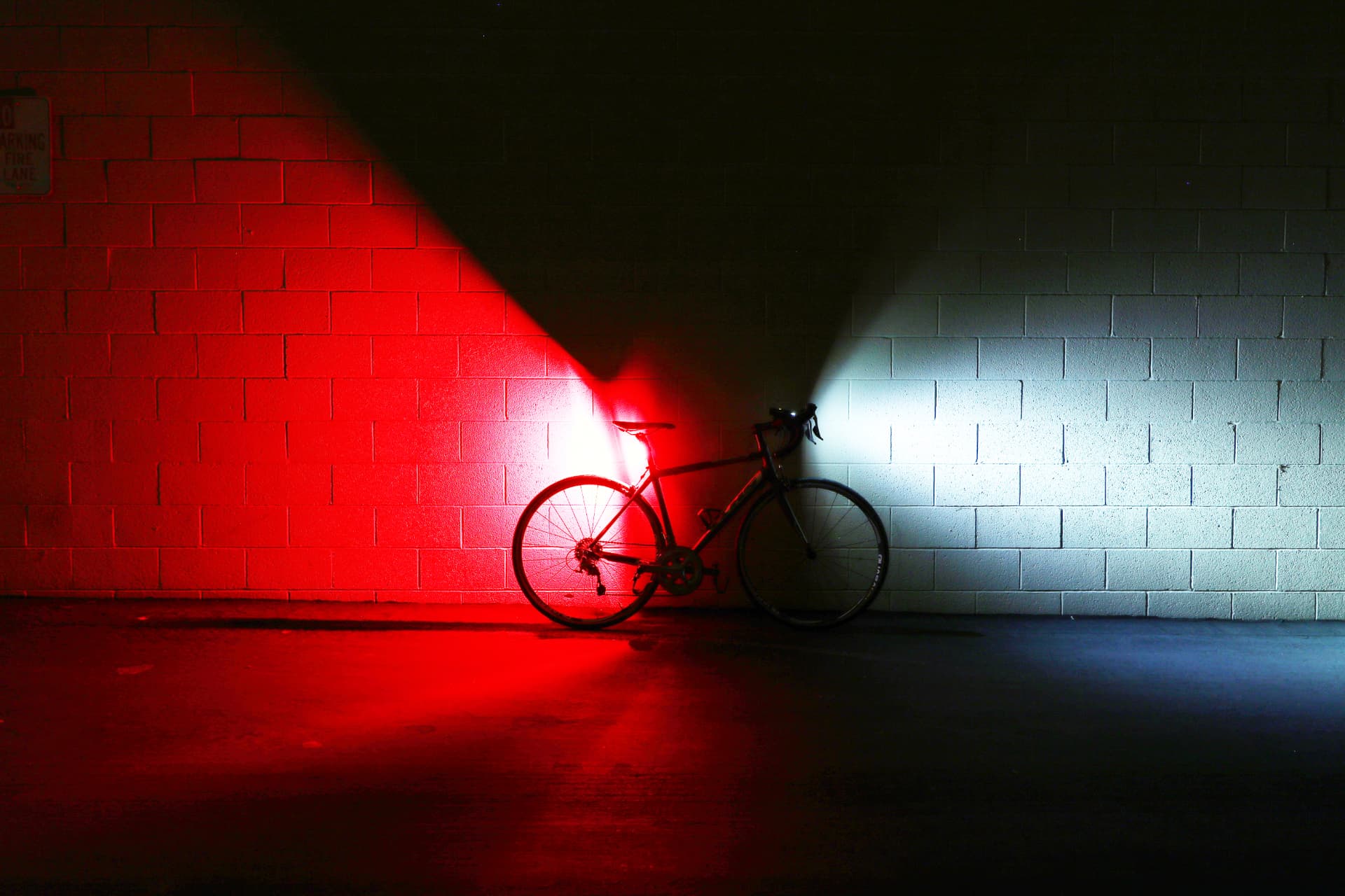 Bicycle lit by a red tail light and a white headlight against a brick wall at night