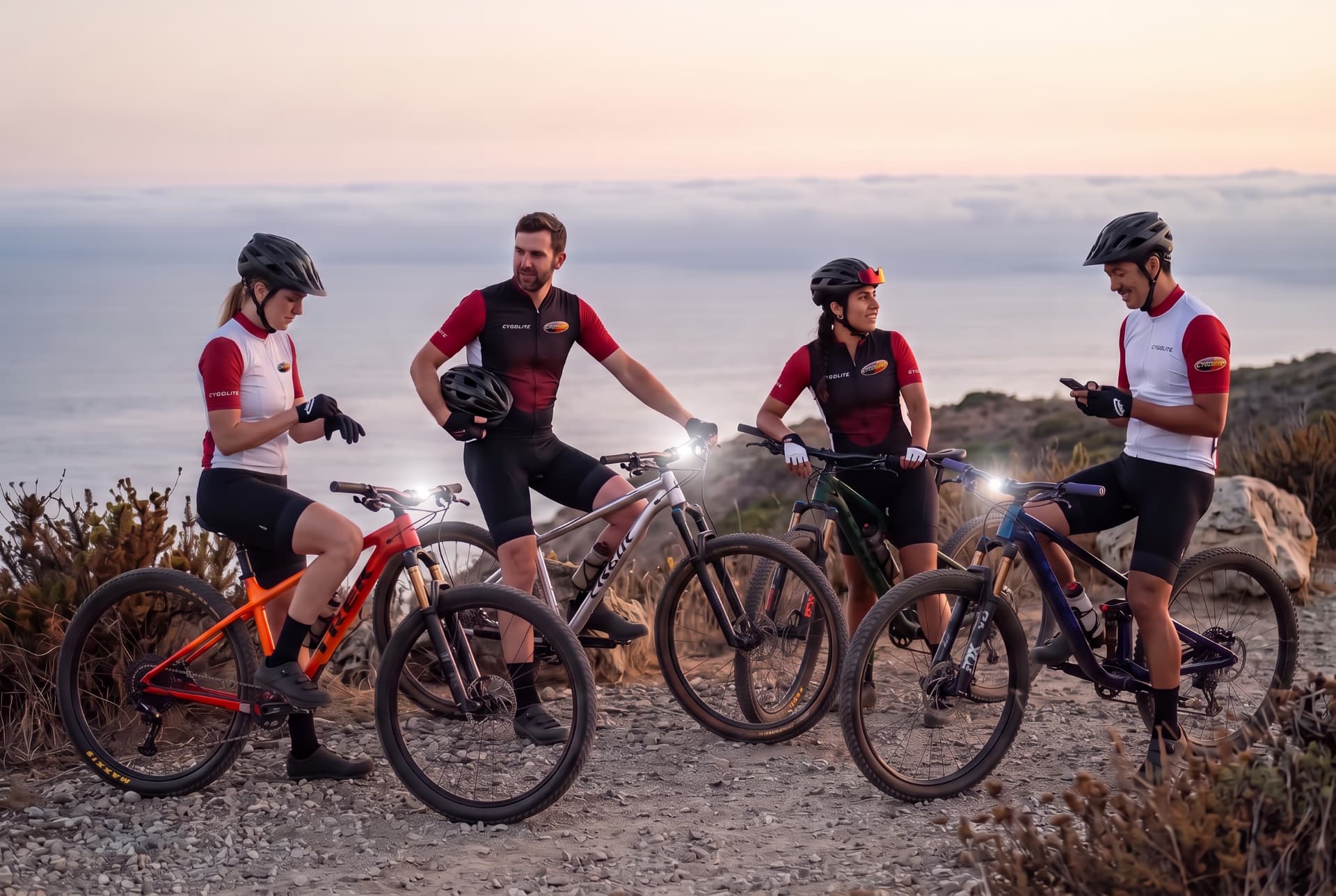 Group of cyclists in Cygolite jerseys with their mountain bikes on a rocky desert ridge at sunset